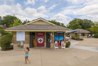 A first aid station and guest services area are shown, with lifeguards seated outside, while a person walks by in swimwear.