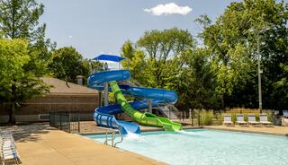 A vibrant water slide cascades into a sunny pool surrounded by greenery and lounge chairs, perfect for summer fun and relaxation.