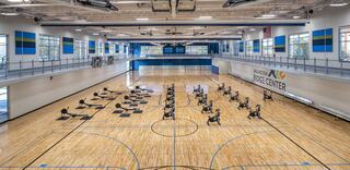 A spacious indoor sports facility features polished wooden floors, multiple exercise bikes arranged in rows, and colorful wall murals.
