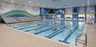 A bright indoor swimming pool features lanes for swimming, with a spectator area and colorful wall designs enhancing the modern atmosphere.