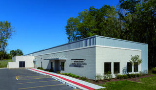 A modern, single-story building with a flat roof, surrounded by greenery and a parking lot, featuring a welcoming entrance and signage.
