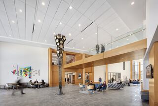 A spacious, modern atrium features wooden accents, contemporary art, and people interacting in a vibrant, open setting.