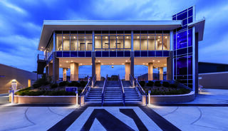 A modern building with large glass windows and a sleek design, featuring stairs, decorative lighting, and a striking blue element at dusk.