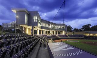 A modern sports facility features sleek architecture and well-designed seating, illuminated against a twilight sky, creating a vibrant atmosphere.