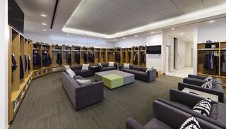 A spacious locker room features comfortable seating, circular arrangement, modern storage units for clothing, and a stylish, sleek design.