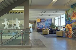 A modern lobby with glass walls features vibrant murals and seating areas where people relax, exuding a creative, inviting atmosphere.