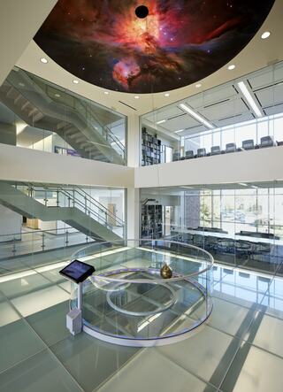 A modern, open space features glass walls, sleek stairs, and a striking celestial mural on the ceiling, creating an innovative atmosphere.