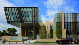 A modern architectural structure features a striking glass canopy, bold lines, and greenery, reflecting contemporary design elements.