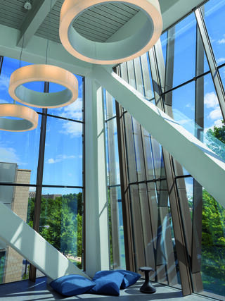 A modern interior with large windows, sleek architecture, and circular light fixtures provides a bright and open atmosphere, complemented by blue cushions.