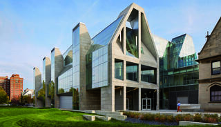 A modern, angular building with glass and concrete, featuring a unique architectural design set against a green lawn and trees.