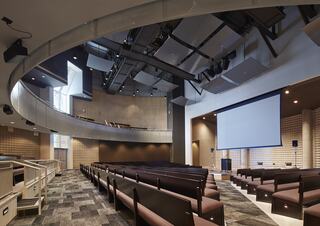 A modern auditorium features curved seating, a large screen, and a sleek design with ample lighting, ideal for presentations and performances.