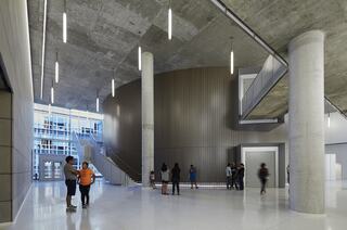 A modern interior space features sleek concrete and metal design, with people engaged in conversation and movement around stylish architecture.