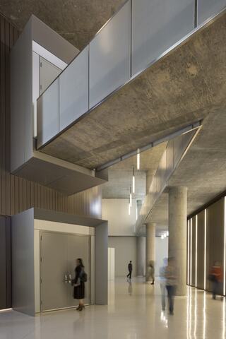 A modern interior features sleek lines, geometric shapes, and a mix of concrete and metal elements, with people moving through the space.