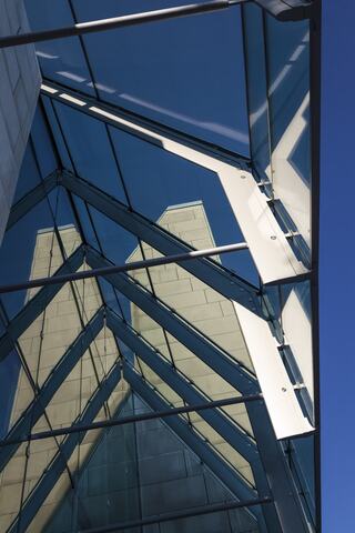 A geometric structure with glass panels reflects the sky and nearby buildings, creating an interplay of light and shadow.
