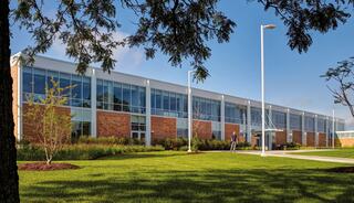 A modern building features large glass windows and brick accents, surrounded by well-maintained landscaping and a clear blue sky.