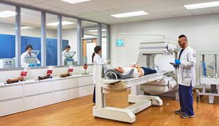 Medical professionals conduct tests in a clinical setting, with a patient lying on equipment and others monitoring from an observation area.