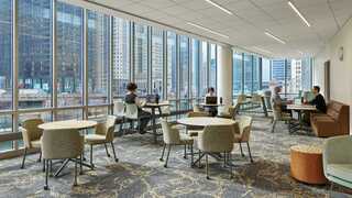 A bright, modern space with large windows, featuring various seating areas where people work and relax amidst a cityscape.