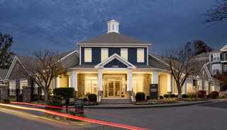 A charming building with modern architecture, illuminated warmly at dusk, surrounded by landscaped gardens and trees.