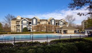 A serene residential area featuring an expansive pool surrounded by well-manicured lawns and cozy apartment buildings under a clear blue sky.