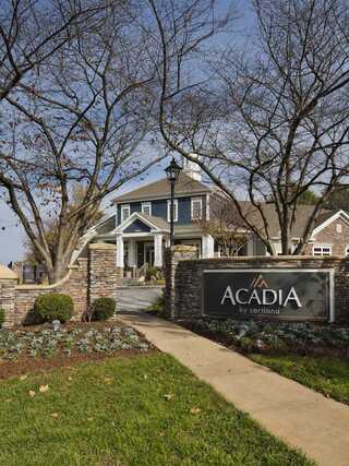 A charming building features stone accents and a welcoming sign for Acadia, surrounded by well-maintained landscaping and trees.