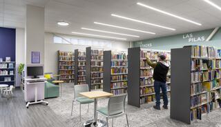 A modern library space features organized shelves of books, reading areas, and a person browsing the shelves, creating a welcoming atmosphere.