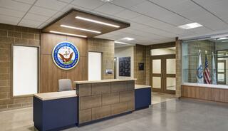 A modern reception area features a wooden desk with an emblem, light wood accents, large windows, and flags prominently displayed.