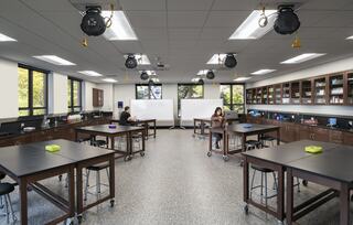 A spacious, well-lit laboratory with dark countertops, mobile tables, shelving, and two people engaged in separate activities.
