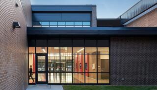 A modern building features a large glass door and windows, showcasing an inviting entryway with sleek lines and a blend of brick and metal.