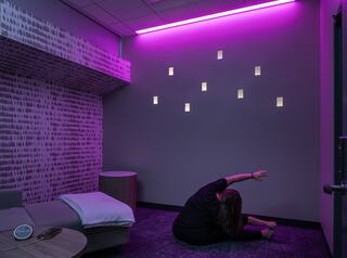 A person stretches on a cozy rug in a softly lit room with purple accent lighting and minimalistic decor, promoting relaxation and tranquility.