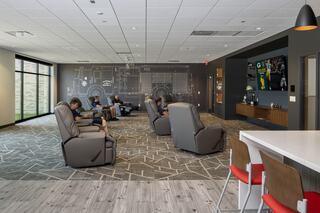 A cozy room features comfortable recliners, large windows, and a wall mural. People relax while watching a screen and enjoying the atmosphere.