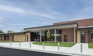 A modern building features large glass windows and a welcoming entrance, surrounded by green grass and a simple concrete walkway.