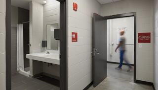 Dedicated apparatus bay toilet/shower room at Concord Township Fire Station 1 features a sink, mirror, and shower. A person walks through an adjacent doorway with signage indicating no turnabout.