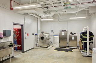 A clean, functional laundry facility with industrial machines, lockers, and firefighter gear on display in a well-lit, spacious room.