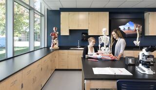 Two students engage in a science lesson surrounded by anatomical models and a microscope in a bright, modern classroom.