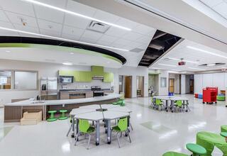 A modern classroom features a bright kitchen area, green furniture, and flexible seating arrangements designed for collaborative learning.