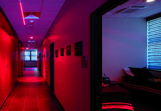 A dimly lit hallway features red lighting, with rooms visible on either side, creating a modern, atmospheric feel.