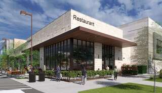 A rec center restaurant with large windows and outdoor seating is set against a clear sky, surrounded by greenery and pedestrian activity.