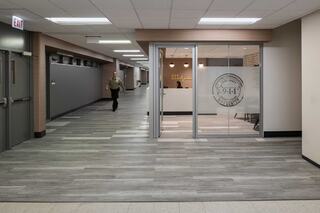 A modern hallway at Cook County 911 Emergency Dispatch Center features gray walls and flooring, with a clear glass office entrance visible, and a person walking in the background.