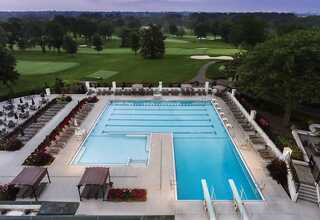 A luxurious pool area features two swimming pools surrounded by lounge chairs and beautifully landscaped gardens, overlooking a golf course.