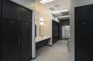 A sleek, modern changing area features dark lockers, a long vanity with mirrors, and bright overhead lighting, creating a spacious atmosphere.