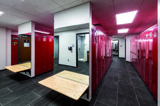 A modern locker room featuring red lockers, wooden benches, and sleek tile flooring under bright lighting.
