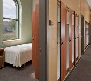 A bright, simple room features a bed and several privacy partitions, likely indicating a shared living space or dormitory.