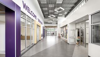 A spacious Caseyville Elementary School lobby and hallways features bright lights, bilingual welcome and bienvenidos signage, and vibrant purple school color, with students entering and moving about.