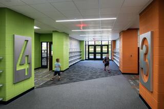 School hallways at Chelsea Intermediate School with green and orange painted walls, each featuring a large, bold metal sign with the number 4 or 3 and two young students crossing paths.