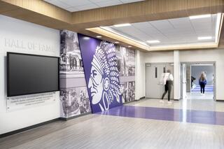 Kaskaskia High School Hall of Fame with neutral colored outlining the ceilings, a digital screen at eye level and a large custom designed wall mural featuring the school district's Kahok Native American inspired graphic logo and images from the community.
