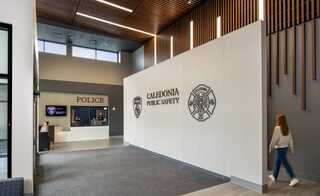 Caledonia, Wiscon's new public safety facility features a police desk and wall displaying Caledonia's police and fire department logos, with a person walking by.
