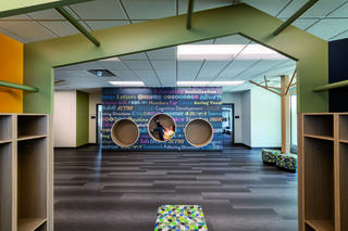 A colorful, spacious community and educational space at Wheeling Park District Recreation Center features playful cubbies, circular sitting nooks on a wall covered with a vibrant custom wall graphic promoting learning and creativity.
