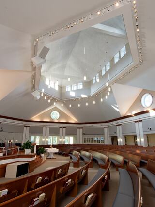 A modern sanctuary features curved wooden pews, large windows, and a unique, angular ceiling with soft lighting, creating a serene atmosphere.