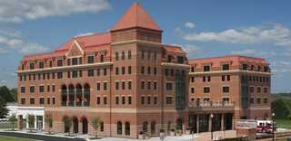 A large, modern brick building features a striking red tiled roof, arched windows, and a welcoming entrance, set against a blue sky.