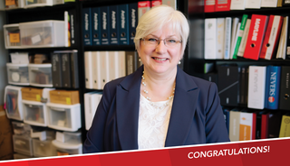 Diane Gilmartin, FGMA CFO, smiling with glasses and short, light hair poses in front of shelves filled with books and binders, with a banner in the corner that reads "Congratulations!"